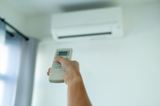 A woman's hand presses the air conditioner remote and points at the air conditioner to operate it.