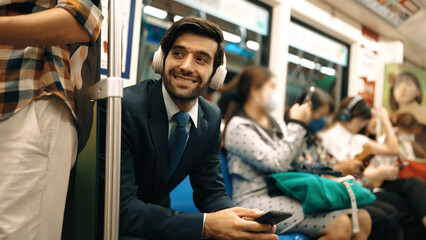 Smiling handsome male investor listening relaxing music while sitting on train. Professional...