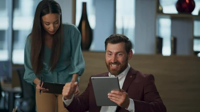 Happy partners winning deal in big open office. Business couple looking tablet
