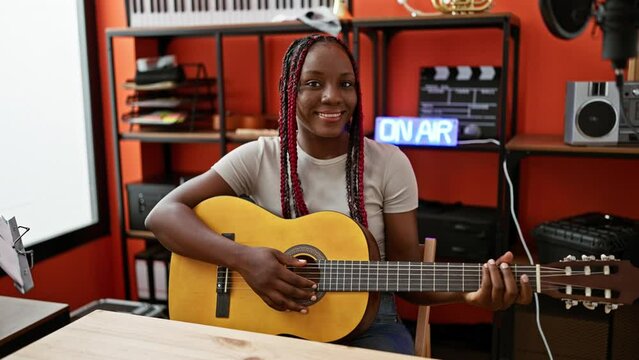 Smiling african american woman plays a classic melody on her guitar indoor. exceptional musician strums chords at music studio while holding an acoustic spanish instrument.