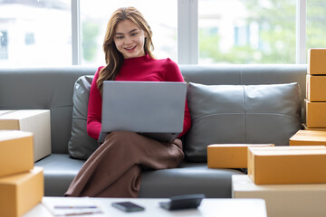 Young Asian woman starting a small online shopping business from home checking internet orders on...