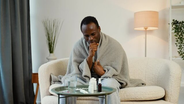 African american sick man coughs sitting wrapped in a plaid on the couch