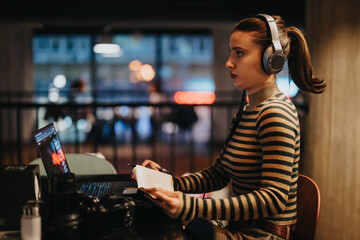 Businesswoman wearing headphones working late at night in the office. She is working on a new...