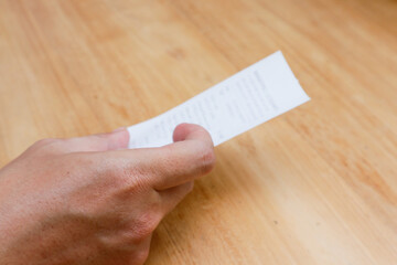 Obraz premium A man's hand is holding a shopping receipt on a wooden table
