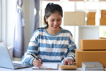 Young Asian woman starts an online shopping business at home using a calculator to calculate costs...