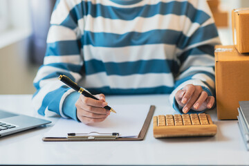 Young Asian woman starts an online shopping business at home using a calculator to calculate costs...