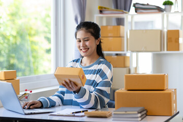 Young Asian woman starting an online shopping business at home using laptop is checking internet...