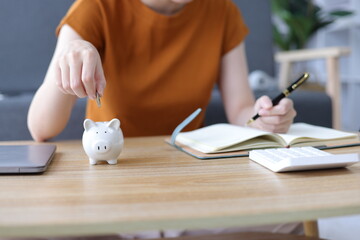 Asian woman putting money into piggy bank at home. Savings, Accounting and Financial Planning