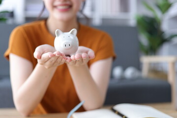 Asian woman putting money into piggy bank at home. Savings, Accounting and Financial Planning