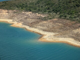 A turquoise body of water meets a rocky shoreline with green vegetation. The water is clear and...