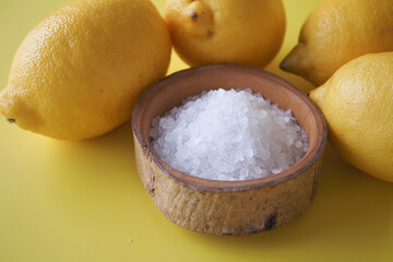 Coarse salt in a bowl and lemon on yellow background 