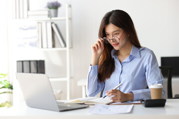 Businesswoman working on financial documents on the desk in the office is writing notes and...