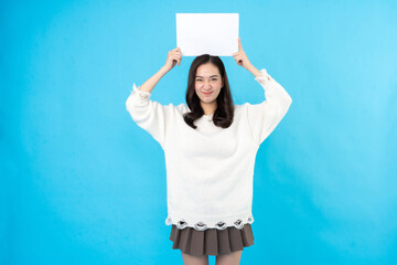 Asian female model with long hair Stand with a white paper sign above your head and leave a space. For inserting text or symbolic words. Taking photos in a studio with a blue background