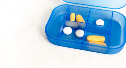 Pastillero azul con píldoras y tabletas comprimidas amarillas y blancas. Organizador de pastillas...