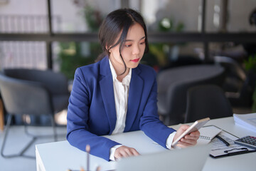 Businesswomen reading financial statistics of new business on smartphone and typing data on laptop while working to analysis strategy investment and management about new startup project in workplace