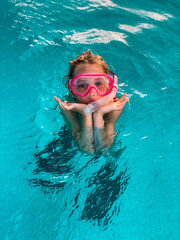 Closeup portrait of cute little girl swimming in the pool with pink snorkelling mask, happy child having fun in the water. Water activities for kids.