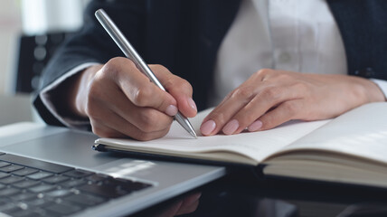 Close up of business woman hand with a pen writing on paper notebook, planning event schedule. Female student online studying on laptop, searching the information, e-learning, online study concept