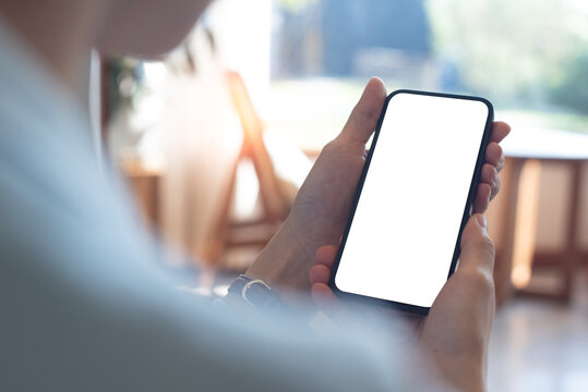 Mockup, woman's hands holding mobile phone with blank screen in coffee shop. Woman using smartphone, looking at the screen, over shoulder view
