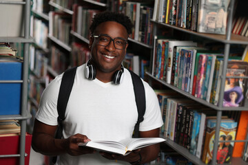 Portrait of african university student doing homework in library and smiling. Happy african american high school student with open book looking at camera while studying for exam