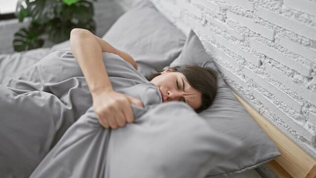 Exhausted yet beautiful young hispanic woman suffering insomnia, lying in the cozy comfort of her bedroom, restless despite the relaxing interior of her home.