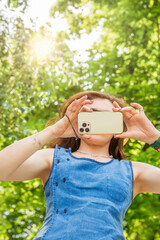 A woman takes a picture in nature with her smartphone. The smartphone covers her face.