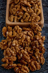 Walnuts in a wooden plate are a source of vegetable protein. Top view of walnut kernel halves in a wooden bowl on a gray background. 