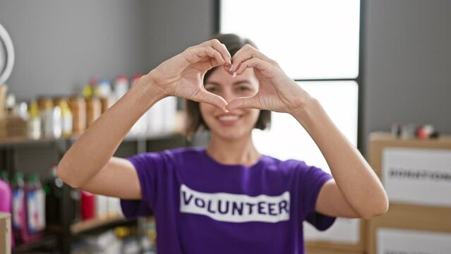 With hands forming a love symbol, a young, beautiful hispanic woman with short hair confidently volunteer at a charity center, her radiant smile reflecting the joy of selfless service.
