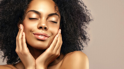 African American skincare model with a glowing healthy skin and curly hair is smiling and posing...