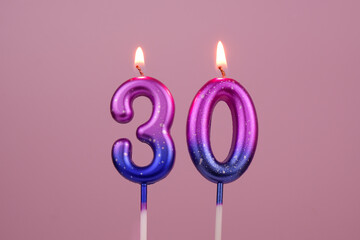 Pink and blue with white spots birthday candles burning on pink background. Number 30.	