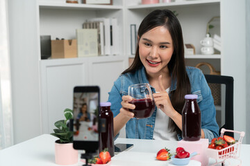 Smiling young beautiful Asian reviewing tasty mixed strawberry and cherry juice detox drinks,...