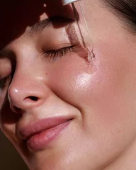Serum. Moisturising and nourishing.  Close up beauty portrait of  beautiful woman with glowing skin is applying a vitamin c skincare product with a pipette dropper. © Beauty Agent Studio