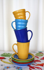 Stack of colorful ceramic tea cups with saucers on the patterned tablecloth