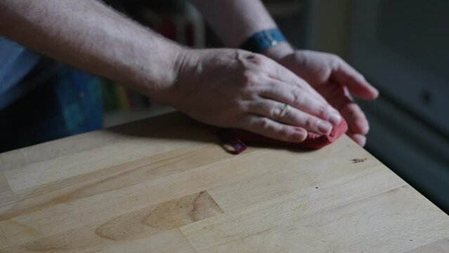 Cleaning crumbs off a butcher's block counter with an orange dish cloth, in a modern kitchen in natural daylight
