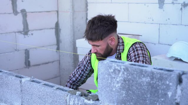 bricklayer installing brick masonry building walls on construction site