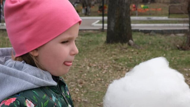 Child girl eating cotton candy outdoors, sweet food	