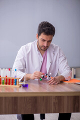 Young male chemistry teacher sitting in the classroom