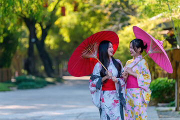 A young woman wearing a Japanese traditional kimono or yukata holding an umbrella is happy and...