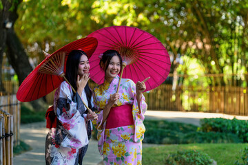 A young woman wearing a Japanese traditional kimono or yukata holding an umbrella is happy and cheerful in the park.