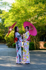 A young woman wearing a Japanese traditional kimono or yukata holding an umbrella is happy and cheerful in the park.