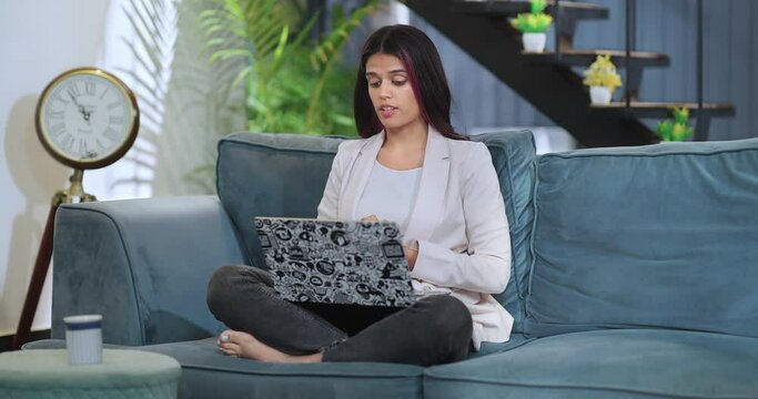 Indian Asian adult busy woman lady staff sitting sofa couch talk online course video call room house young female girl office sales agent worker do work from home job speak client laptop look screen
