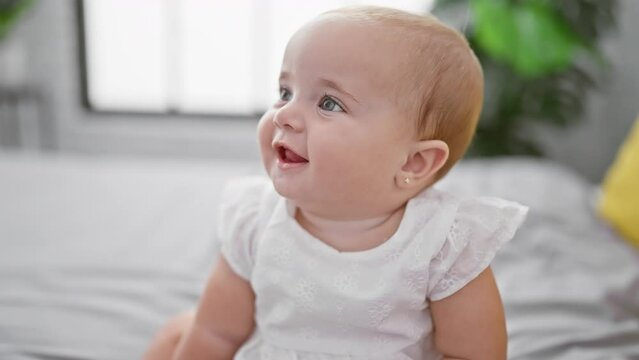 Adorable newly awake baby relaxed, sitting on bed, smiling broadly in cozy bedroom comfort