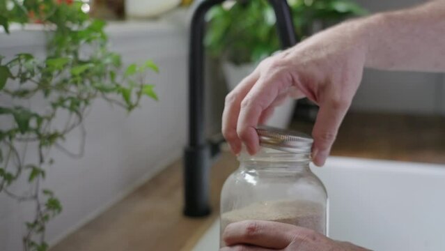 Opening a jar of psyllium husk fiber, spooning some into a glass of water and stirring it, in a farmhouse kitchen, in natural daylight
