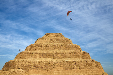 Fototapeta na wymiar Paragliders in the blue sky above the oldest stone building in the world - the step pyramid of king Djoser in Saqqara, Egypt