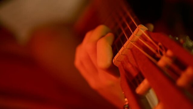 Cinematic dark red color, close up professional classical guitar, teenager hands playing, 4K slow motion. Neck of the guitar