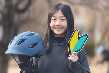 自転車用ヘルメットと初心者マークを持つ女の子 - obrazy, fototapety, plakaty