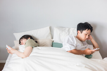 ベッドの中にいるスマホ依存の不仲の夫婦
