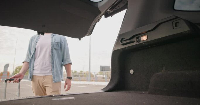 Young man opens Car Trunk and puts suitcase in