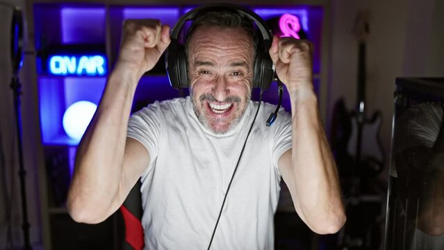 Cheerful middle age man with grey hair ecstatically celebrates his win on a video game stream in a dark gaming room