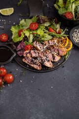 sliced grilled Organic Tuna Steak on black ceramic serving dish with salad on a table
