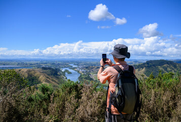 Man taking photos using smartphone of Huntly and the north Waikato lakes. Hakarimata Summit Track. Huntly. New Zealand.